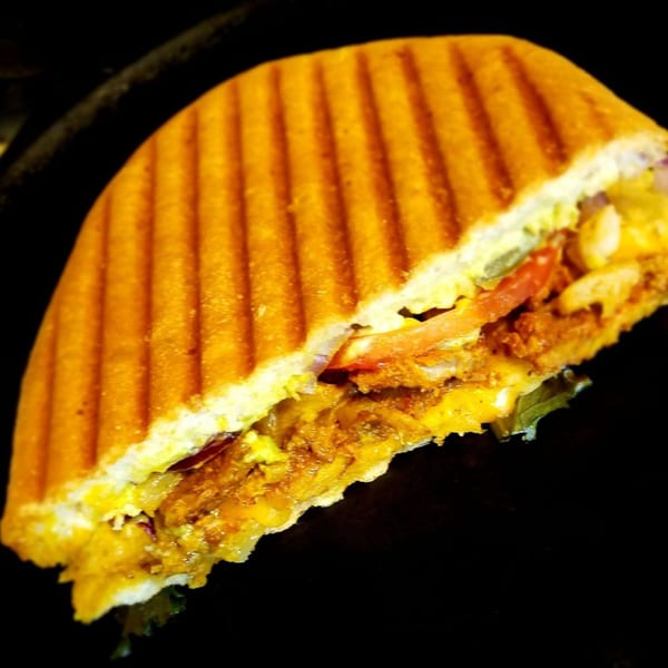 A grilled panini sandwich, cut in half, revealing melted cheese, meat, and vegetables.