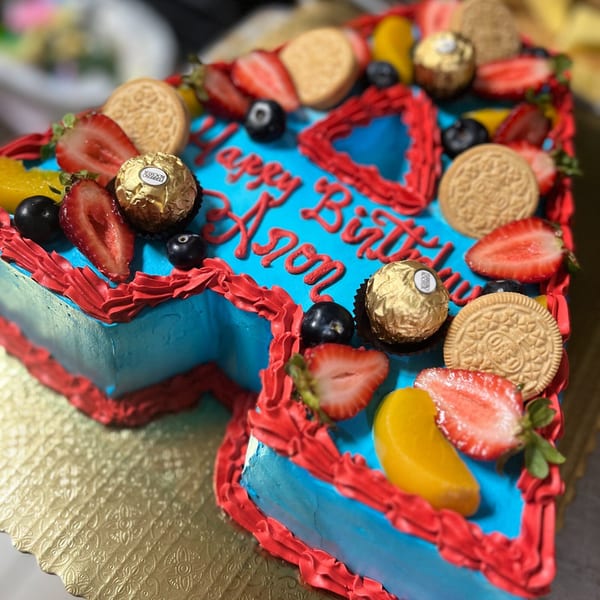 A vibrant blue birthday cake with red frosting, topped with strawberries, blueberries, cookies, and chocolates.