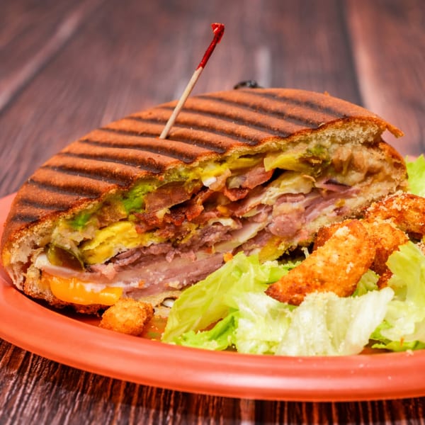 A grilled panini sandwich, cut in half, revealing layers of meat, cheese, and avocado, served with a side salad.