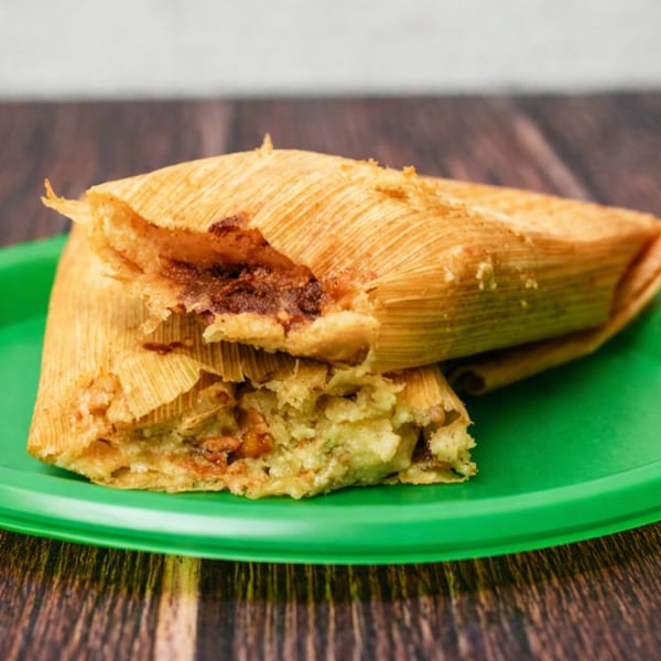 Two Los Tarascos tamales, one partially unwrapped to show the savory filling, on a green plate.
