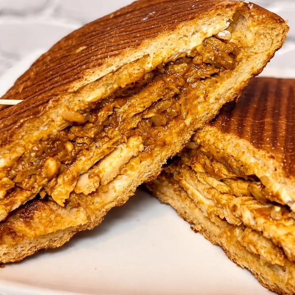 Close-up of a grilled panini sandwich, cut in half, revealing a savory chicken and onion filling.